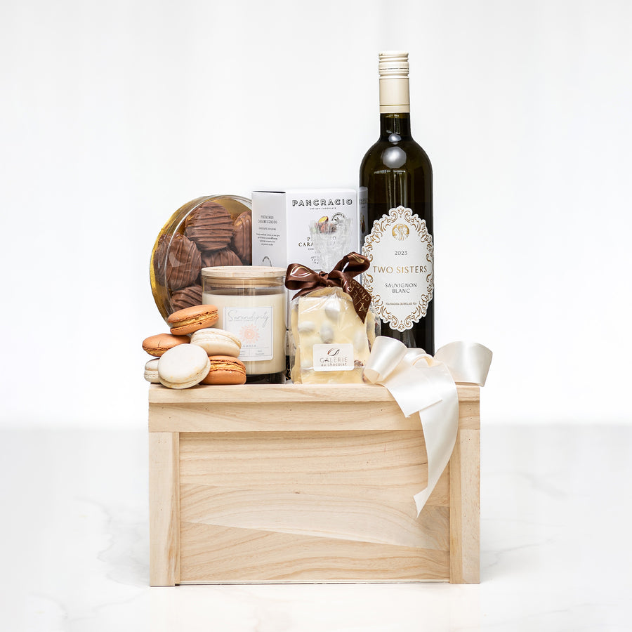 Sophisticated Sweets gift with macarons, cookies, a candle and a bottle of white wine on a crate