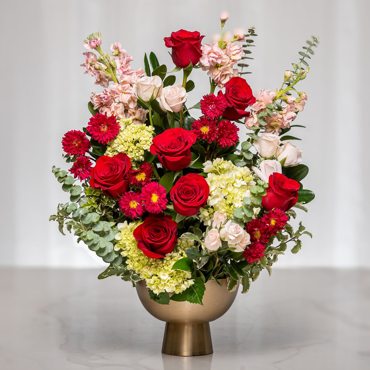 Sweet Serenade arrangement of red roses, gerberas and mixed blooms in a gold footed vase