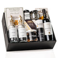 The Gourmet Edit: a black wood crate with glass oil and vinegar bottles with gold pour spouts, a bottle of Poggio Pasano Primitivo, Castello brie, Kanel seasonings, chutney and a jar of shortbread