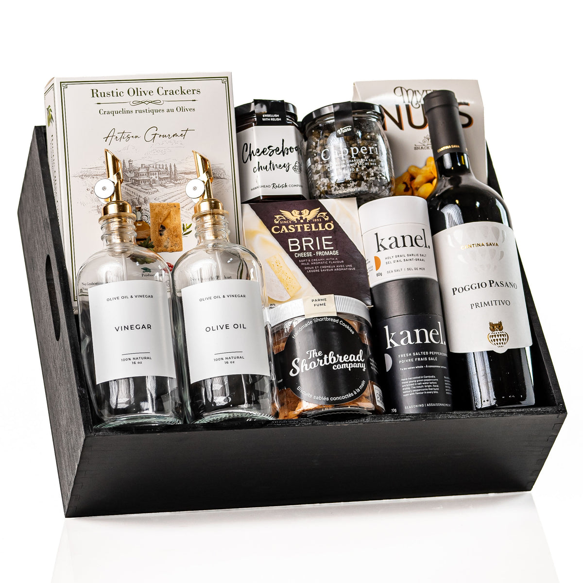 The Gourmet Edit: a black wood crate with glass oil and vinegar bottles with gold pour spouts, a bottle of Poggio Pasano Primitivo, Castello brie, Kanel seasonings, chutney and a jar of shortbread