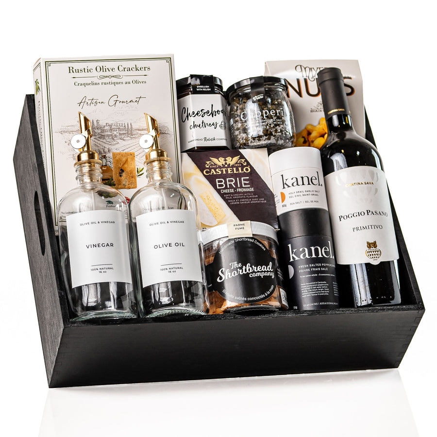 The Gourmet Edit: a black wood crate with glass oil and vinegar bottles with gold pour spouts, a bottle of Poggio Pasano Primitivo, Castello brie, Kanel seasonings, chutney and a jar of shortbread