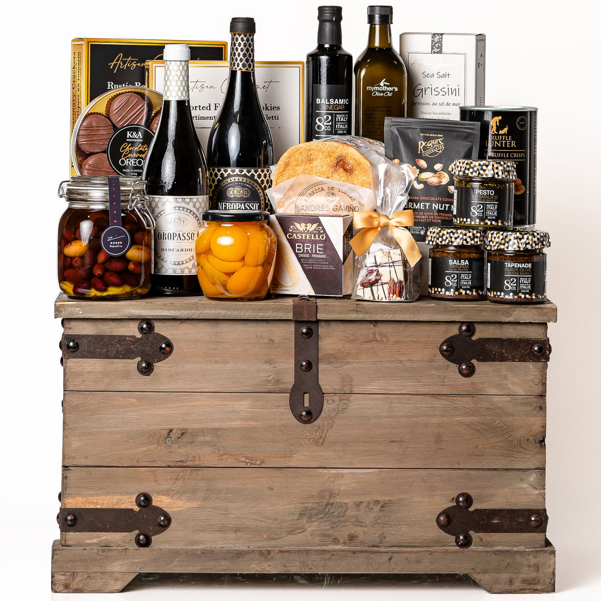 Treasure Trove Large: a rustic wooden trunk with black metal detailing overflowing with Biscardo wines, My Mother's olive oil and olives, balsamic vinegar, peach halves, chocolate covered Oreos, Castello brie and Co. 82 jars