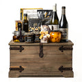 Treasure Trove Medium: a rustic wooden trunk with black metal detailing holding Biscardo Neropasso and OroPasso wines, My Mother's olive oil and olives, peach halves, Castello brie and Co. 82 jars