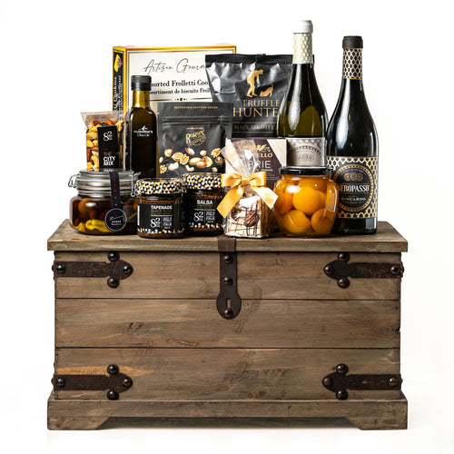 Treasure Trove Medium: a rustic wooden trunk with black metal detailing holding Biscardo Neropasso and OroPasso wines, My Mother's olive oil and olives, peach halves, Castello brie and Co. 82 jars