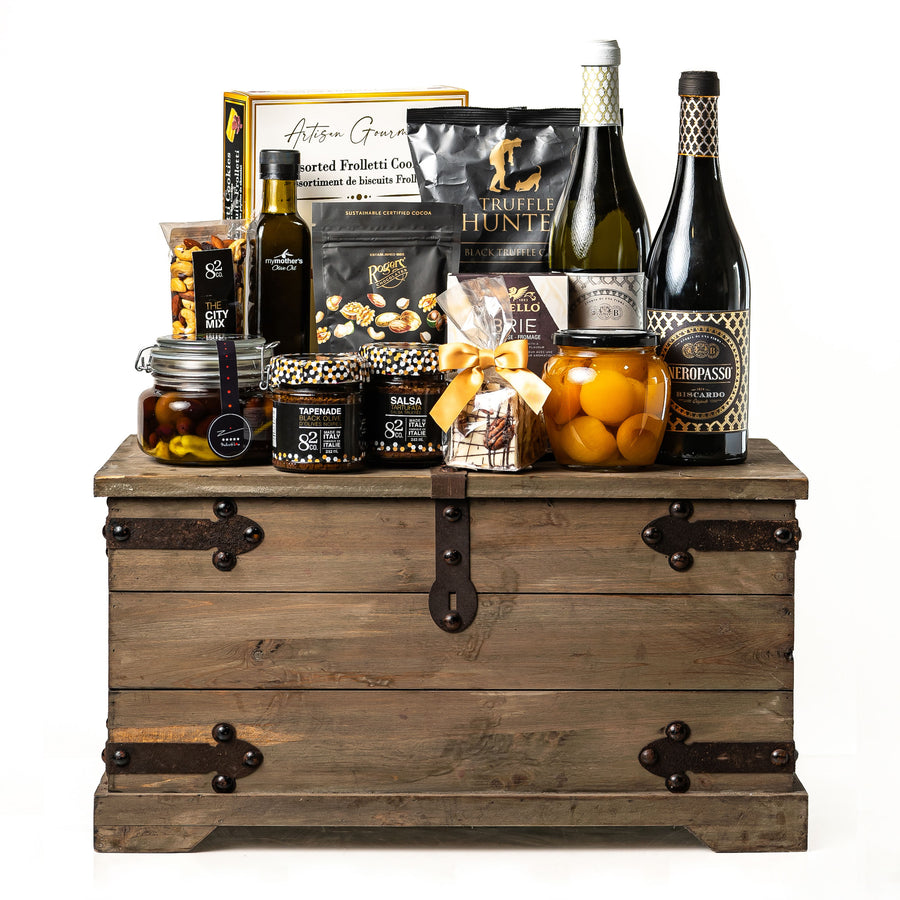 Treasure Trove Medium: a rustic wooden trunk with black metal detailing holding Biscardo Neropasso and OroPasso wines, My Mother's olive oil and olives, peach halves, Castello brie and Co. 82 jars