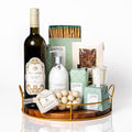 Unwine'd: a round wood tray with gold edging holding a bottle of Two Sisters Sauvignon Blanc, Lucia No. 7 hand and body lotion, soy candle, bar soap and matches, yogurt covered blueberries and a Donini chocolate bar