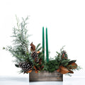 Woodland Grace and Glow arrangement with green taper candles, pine cones and magnolia in a wooden box