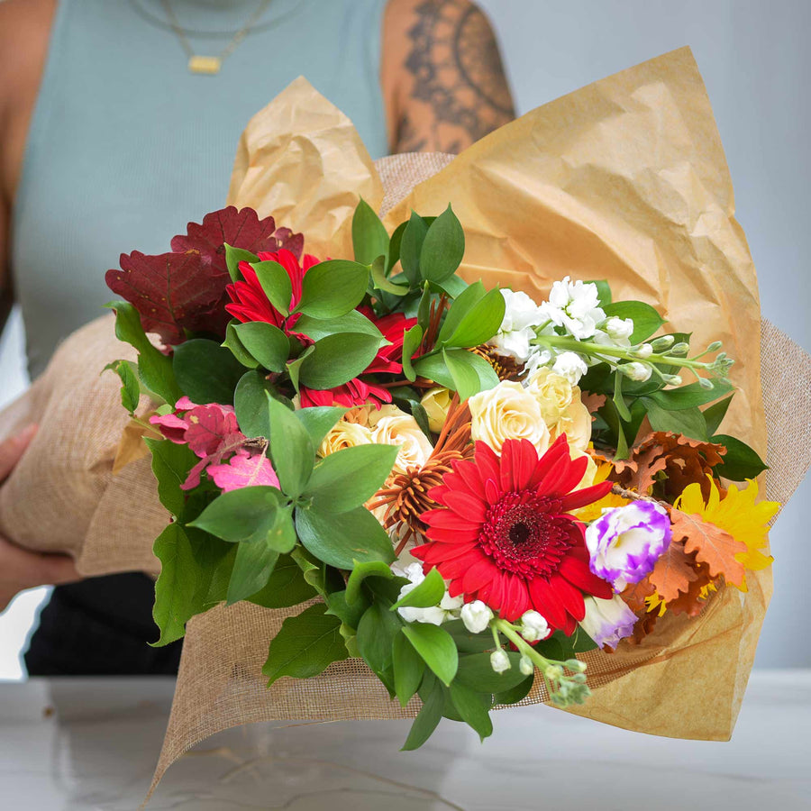 Hand tied spring and summer bouquet of gerberas, roses and mixed blooms wrapped in kraft paper