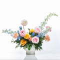 Whispering Petals arrangement of blue delphinium, peach roses and ranunculus in a white pot