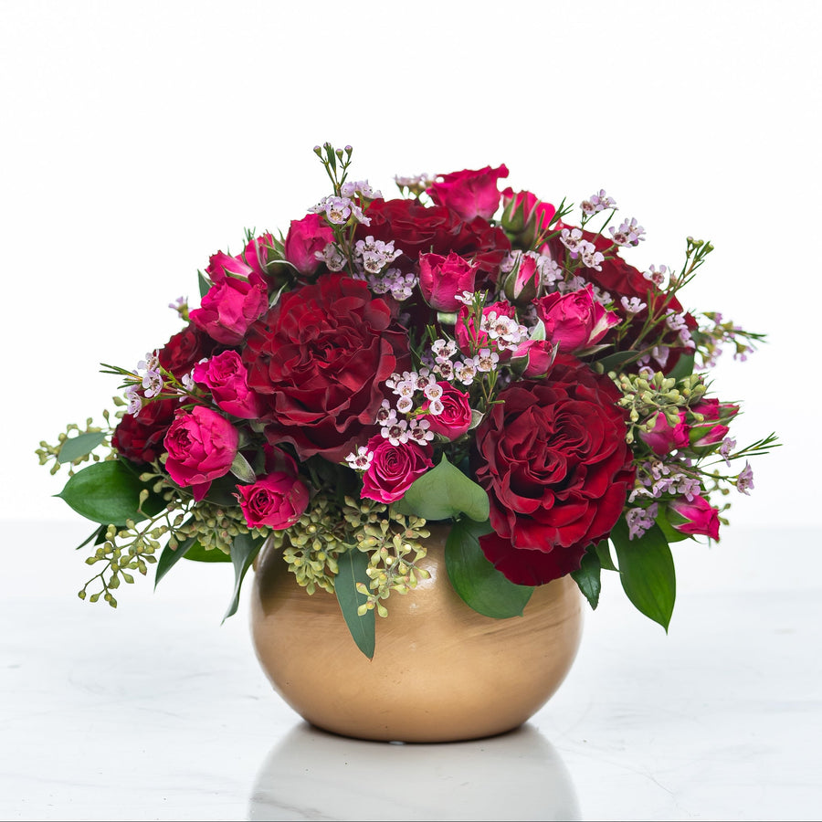 Rosalina arrangement of magenta and burgundy roses with wax flower in a gold footed bowl