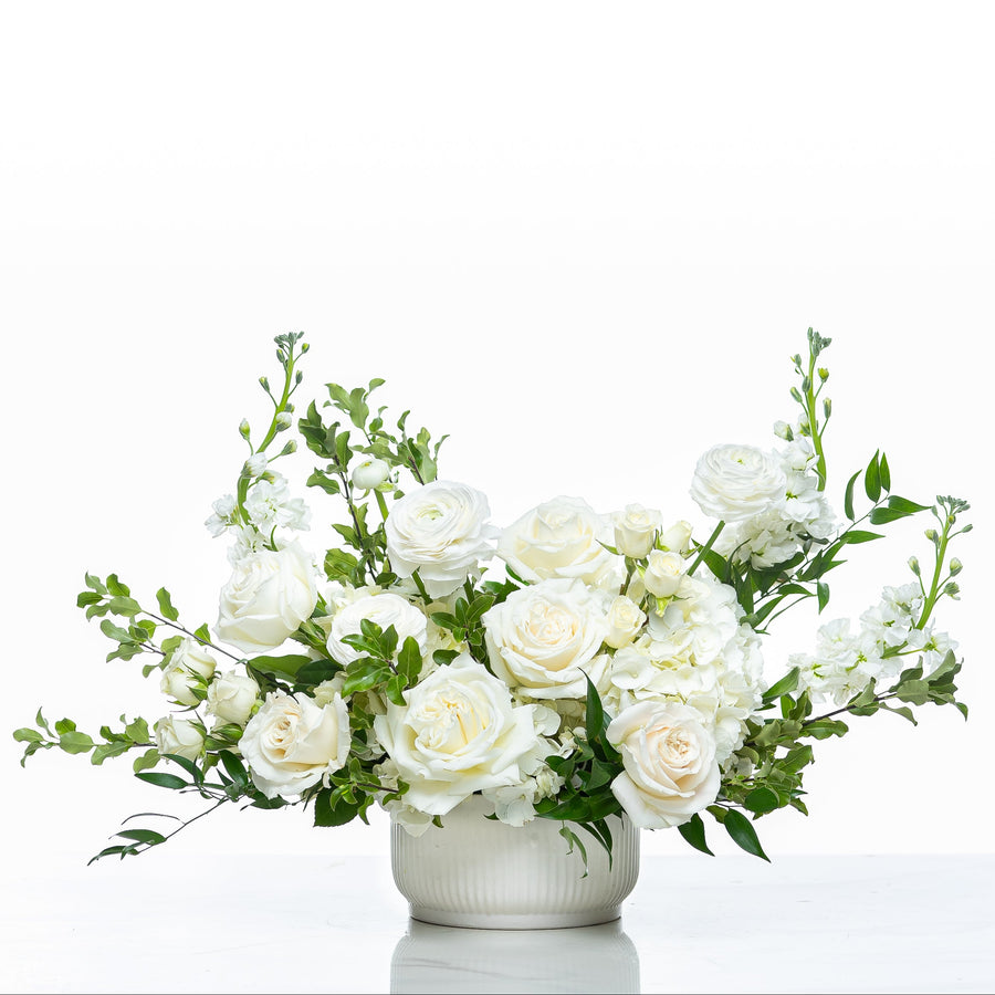 Angelic arrangement of white roses, stock and delphinium in a fluted white pot