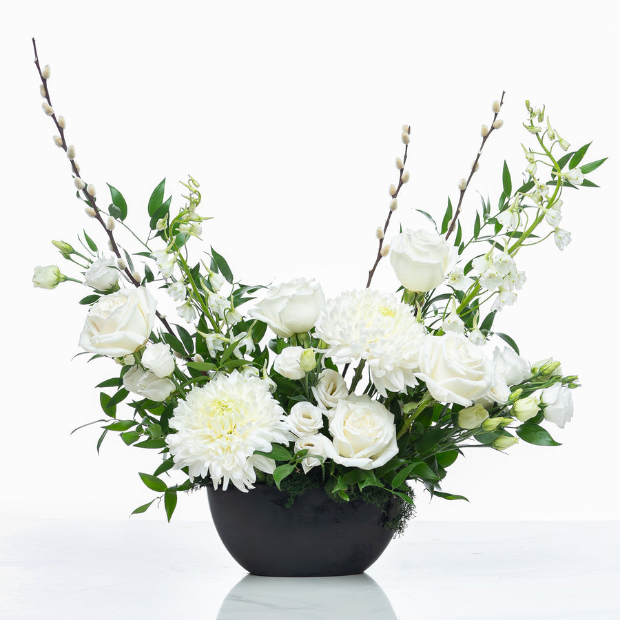 Posh arrangement of white roses, carnations and orchids in a black footed bowl