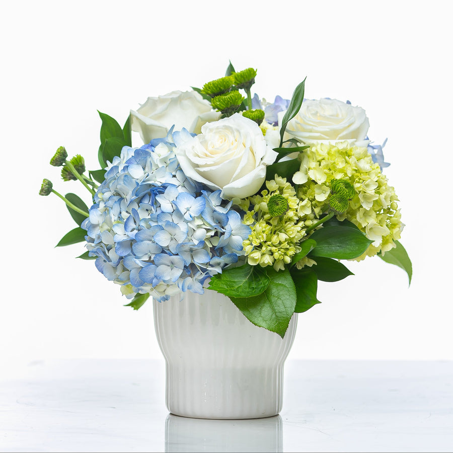 Charming arrangement of blue hydrangea, white roses and green hydrangea in a fluted white pot