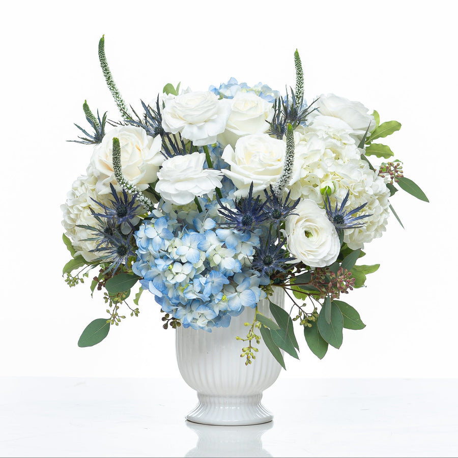 Blue Skies arrangement of blue hydrangea, white roses and thistle in a white footed vase