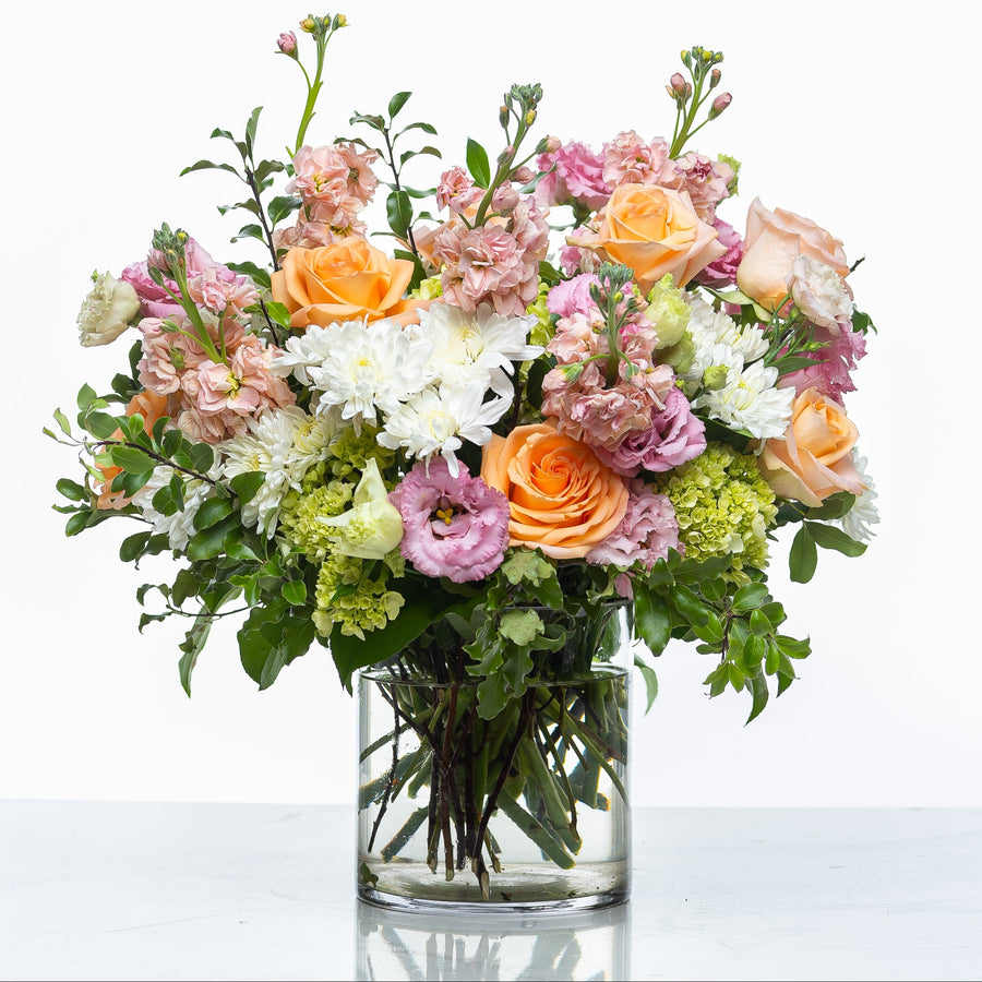 Pretty Petal arrangement of peach roses, stock and lisianthus in a clear glass vase
