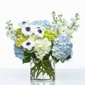 Azure arrangement of blue hydrangea, white anemones and stock in a clear glass vase
