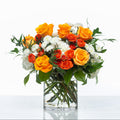 Sunset arrangement of orange roses and white chrysanthemums in a clear glass cylinder vase