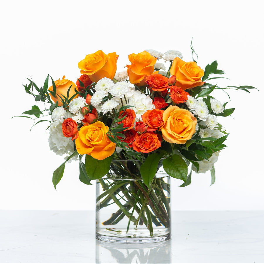 Sunset arrangement of orange roses and white chrysanthemums in a clear glass cylinder vase