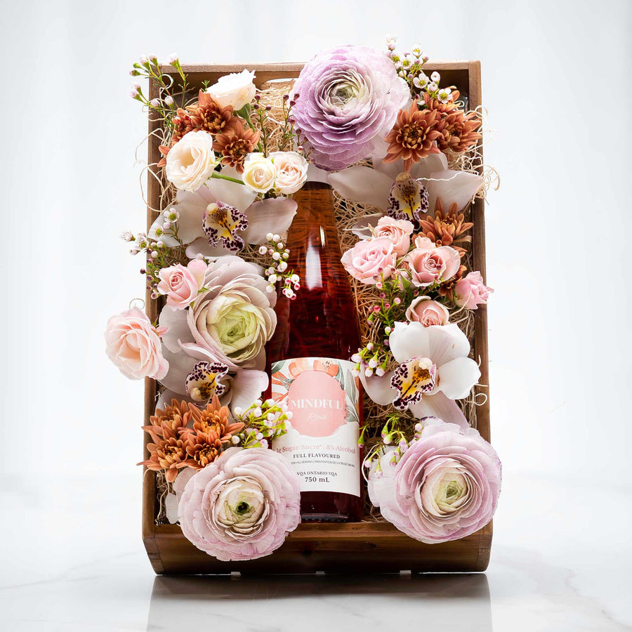 Tranquility floral gift crate of pink roses and ranunculus arranged around a bottle in a wooden box
