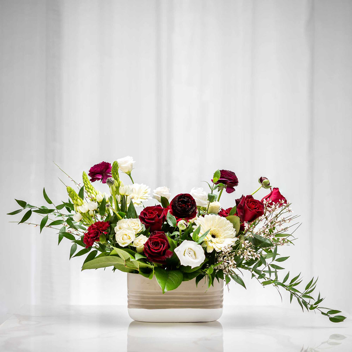 Vibrations floral arrangement of burgundy and white roses with greenery in a cream ceramic pot